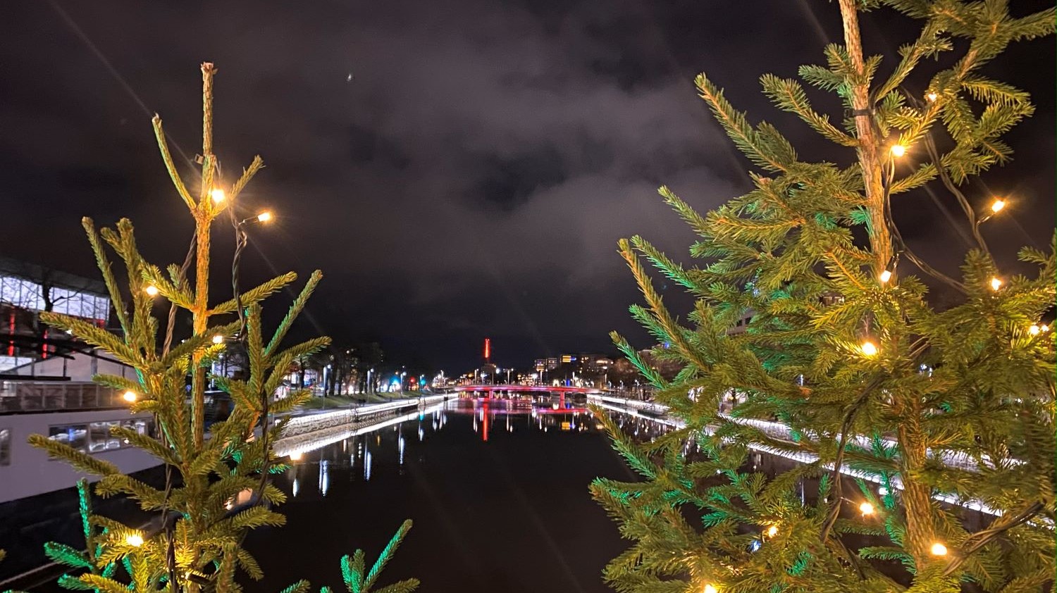 Juhlavalaistuja kuusipuita kaupunkijoen äärellä